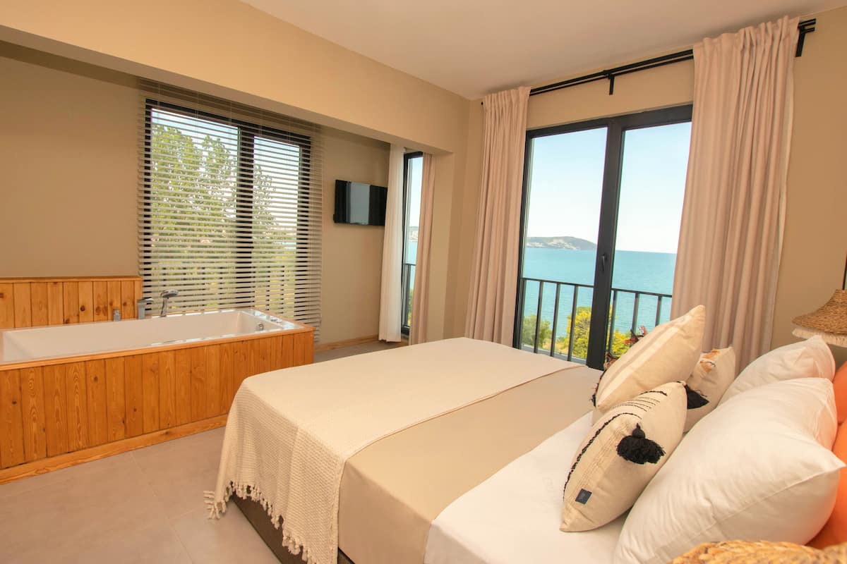 A bedroom with a large bed, a wooden bathtub, and a view of the sea.