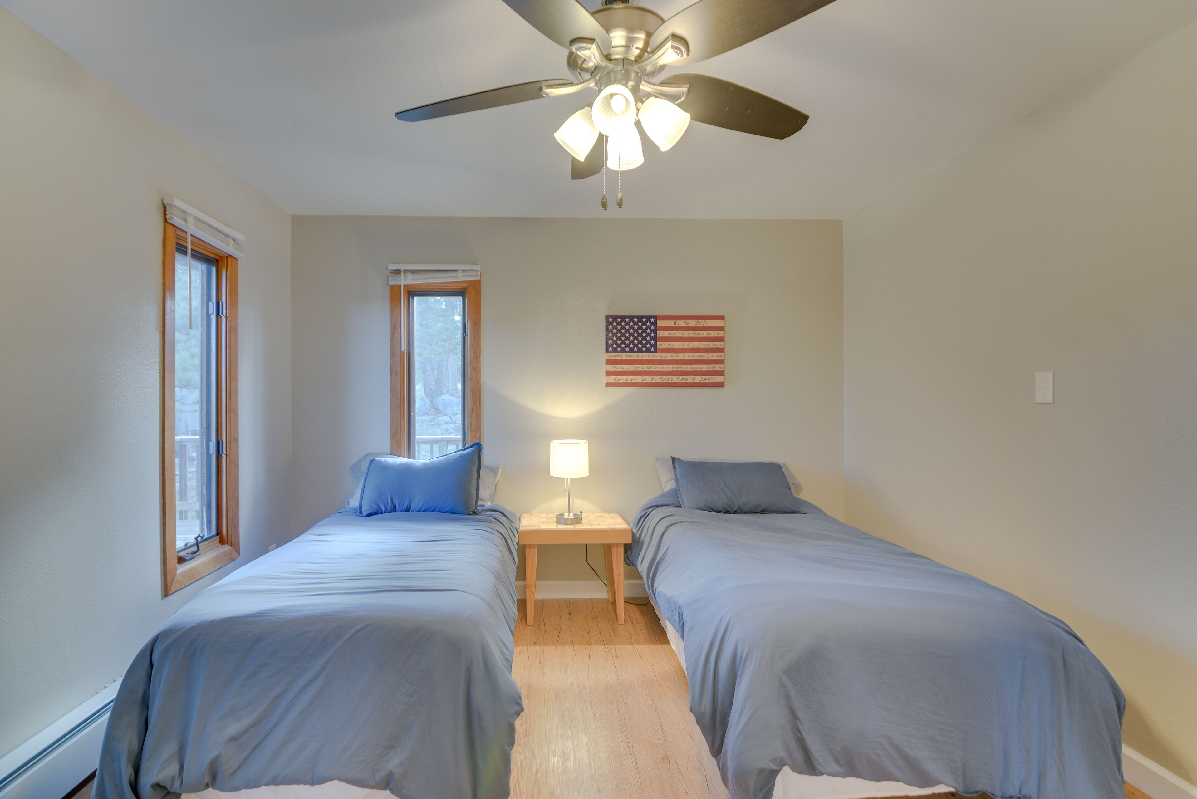 A bedroom with two beds, a ceiling fan, a nightstand with a lamp, and an American flag on the wall.