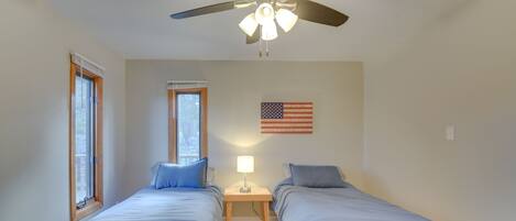 A bedroom with two beds, a ceiling fan, a nightstand with a lamp, and an American flag on the wall.