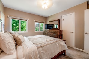 Ein Schlafzimmer mit Bett, Kommode, Fernseher und Fenstern.