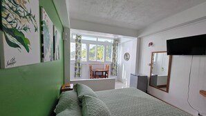 A bedroom with a bed, a desk, a chair, a television, and a window with curtains.