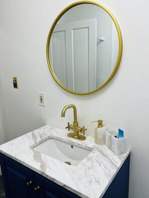 A bathroom with a white marble sink, gold faucets, a gold-framed mirror, and dark blue cabinets. - DOWNTOWN, Rupp Arena just 5 min away. 2 bedr/1 Bath cozy home. (Lexington)
