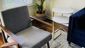 A living room with a grey armchair, a small round table, a blue sofa, and a potted plant.