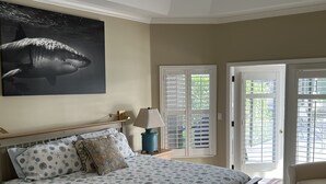 Een slaapkamer met een bed, nachtkastje, lamp, deur en uitzicht op de omgeving.