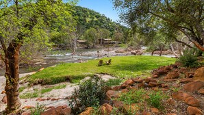 Una propiedad junto al río con césped, rocas y una cabaña de madera.