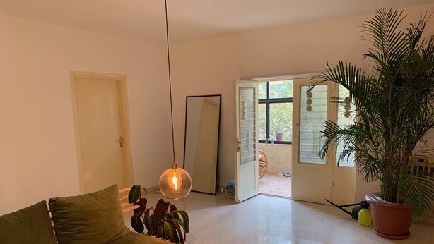 Un salon avec un canapé vert, un luminaire suspendu, un grand miroir et une plante en pot.