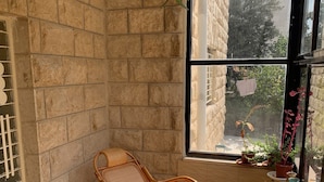 Une pièce d’angle avec un fauteuil en osier, une fenêtre donnant sur un paysage verdoyant et un sol carrelé.
