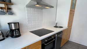 A modern kitchen with a black induction cooktop, a coffee maker, wooden cabinets, and a stainless steel sink. - Charming 1-bed for 4 pers with Sauna, WiFi, and Private Parking (Valloire)