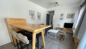 A compact living space with a wooden dining table, black bar stools, a white coffee table, a television, and framed pictures on the walls. - Charming 1-bed for 4 pers with Sauna, WiFi, and Private Parking (Valloire)