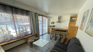 A modern living room with a sofa, a coffee table, and a dining area with a kitchen in the background. - Charming 1-bed for 4 pers with Sauna, WiFi, and Private Parking (Valloire)