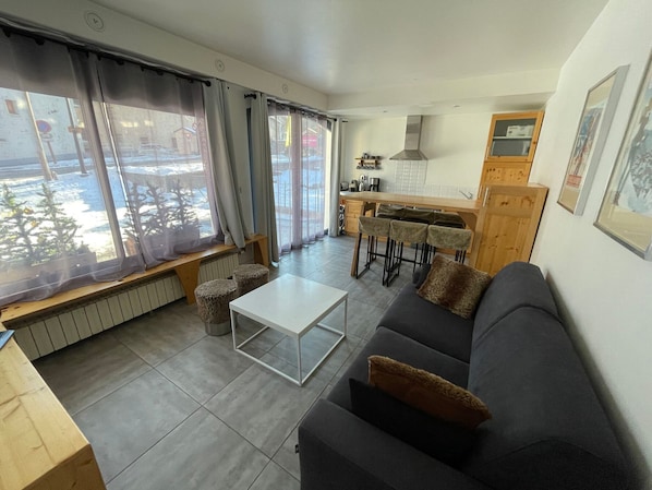 A modern living room with a sofa, a coffee table, and a dining area with a kitchen in the background.