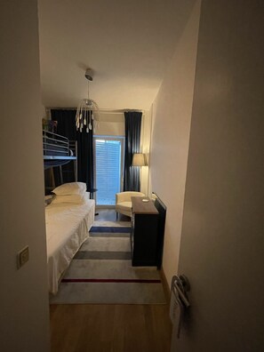 A hotel room with a bunk bed, a desk, a chair, a lamp, and a view of the outside.