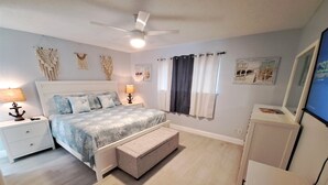Une chambre à coucher comprenant un lit, des tables de chevet, un ventilateur de plafond, un banc et une commode.