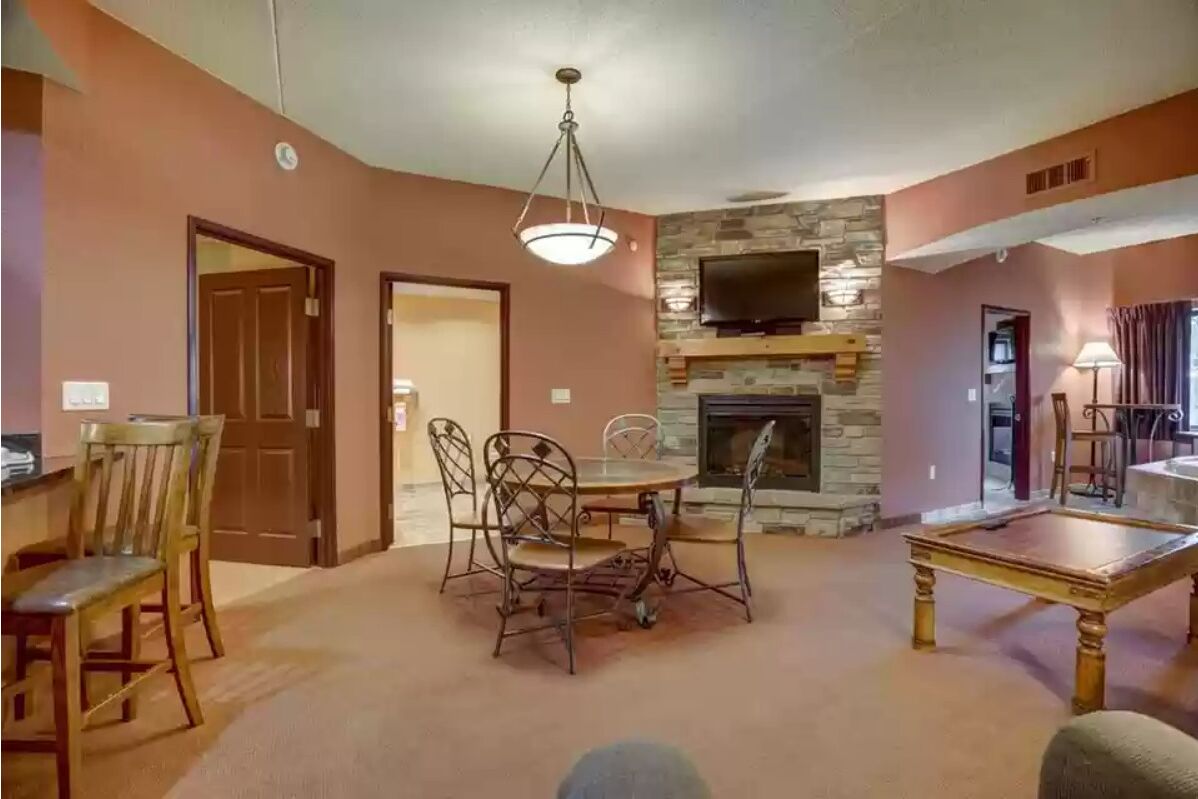 A living room with a stone fireplace, a dining table with chairs, and a television mounted on the wall.