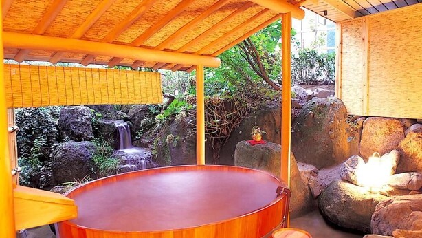 A traditional Japanese onsen with a wooden hot tub, a stone waterfall, and a wooden structure with a tiled roof. - yuzawahotel (Yuzawa)