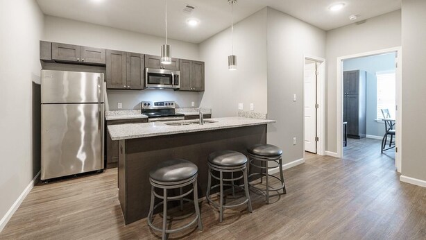 A modern kitchen with stainless steel appliances, a granite countertop, and a bar stool area. - Luxury Furnished Rental in Conway, AR Unit 206 (Conway)