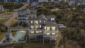 Ein mehrstöckiges Haus mit Pool, umgeben von einer Wohngegend mit Blick auf das Meer bei Sonnenuntergang.