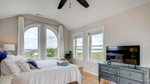 Ein Schlafzimmer mit einem großen Bett, einem Schminktisch, einem Fernseher und großen Fenstern mit Blick.