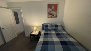 A bedroom with a checkered bedspread, a bedside lamp, a door, and a painting on the wall. - Stylish Duplex with an Equine View (Indian Trail)