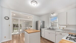 Una cocina moderna con armarios blancos, encimera de madera y electrodomésticos de acero inoxidable, con vistas al exterior.