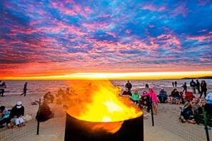 Escena de playa con un hogar para fuego al frente y gente reunida alrededor.