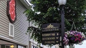 Vista de la calle con una cafetería, un cartel que anuncia Waterfront Park y otro que indica Downtown Ludington.