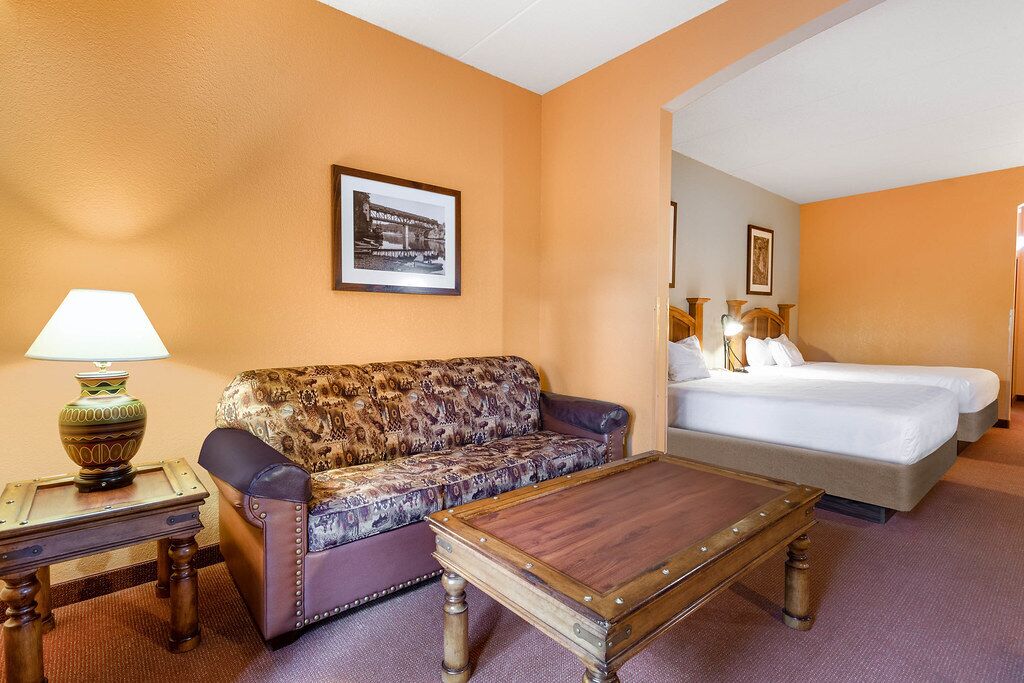 Une chambre d’hôtel avec un canapé, une table basse en bois, un lit avec deux oreillers et un tableau encadré au mur.