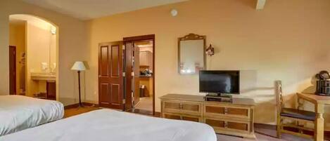 A hotel room with two beds, a television, a desk with a chair, a mirror, and a wardrobe.