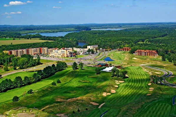 Golfkenttä, jossa on klubitalo, pysäköintialue ja suuri rakennuskompleksi taustalla.