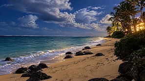 Una playa con rocas, palmeras y olas del océano.