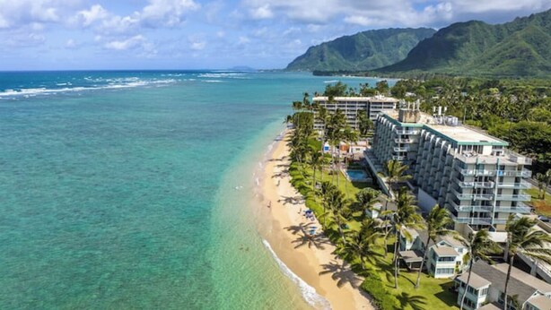 A beachfront hotel with multiple buildings, a sandy beach, and a clear view of the ocean. - Island Life Retreat-Ocean Front-Beach Access (Hauula)