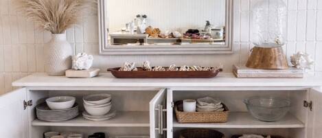 A white cabinet with shelves containing bowls, mugs, and baskets.