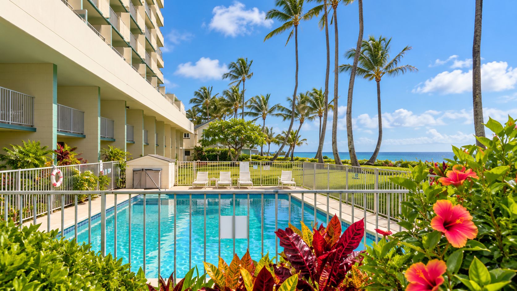 A swimming pool surrounded by lush greenery and palm trees, with a view of the ocean.
