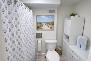 Een badkamer met douchegordijn, toilet, wastafel en een foto met strandthema aan de muur.