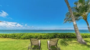 Two lounge chairs facing a view of the ocean with a palm tree and a hedge in the foreground. - Island Life Retreat-Ocean Front-Beach Access (Hauula)