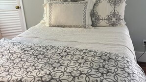 A bed with a patterned bedspread, two pillows with a leaf design, and a white door with a brass doorknob.