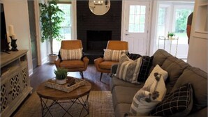 A cozy living room with a fireplace, two armchairs, a sofa, and a coffee table with a plant.