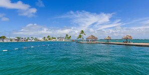 Un resort costero con construcciones de techo de paja, un muelle y un cielo azul despejado.
