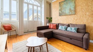 A living room with a brown sofa, a wicker chair, and a small table. - GuestReady - Bolhão Market Place (Porto)