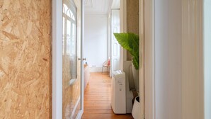 A narrow hallway with wooden flooring, a white radiator, and a large green plant. - GuestReady - Bolhão Market Place (Porto)