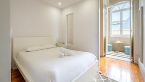 A bedroom with a large bed, a door, and a view of the outside. - GuestReady - Bolhão Market Place (Porto)