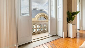 A room with a wooden floor, a white radiator, and a view of a balcony with a stone balustrade. - GuestReady - Bolhão Market Place (Porto)