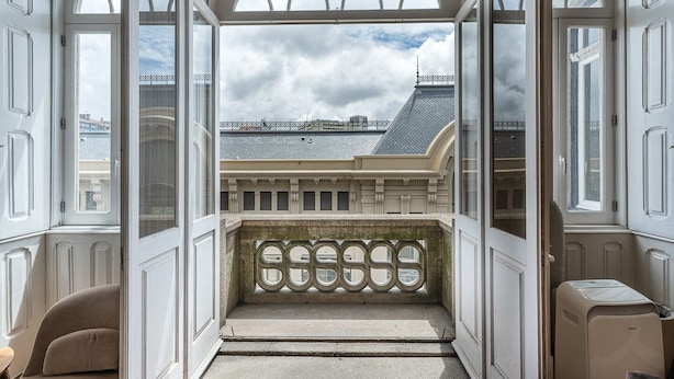 A view from a balcony with a stone balustrade, looking out over a cityscape with buildings and a cloudy sky. - GuestReady - Bolhão Market Place (Porto)