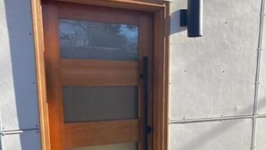 A modern door with a wooden frame and frosted glass panels, a black handle, and a green planter next to it.