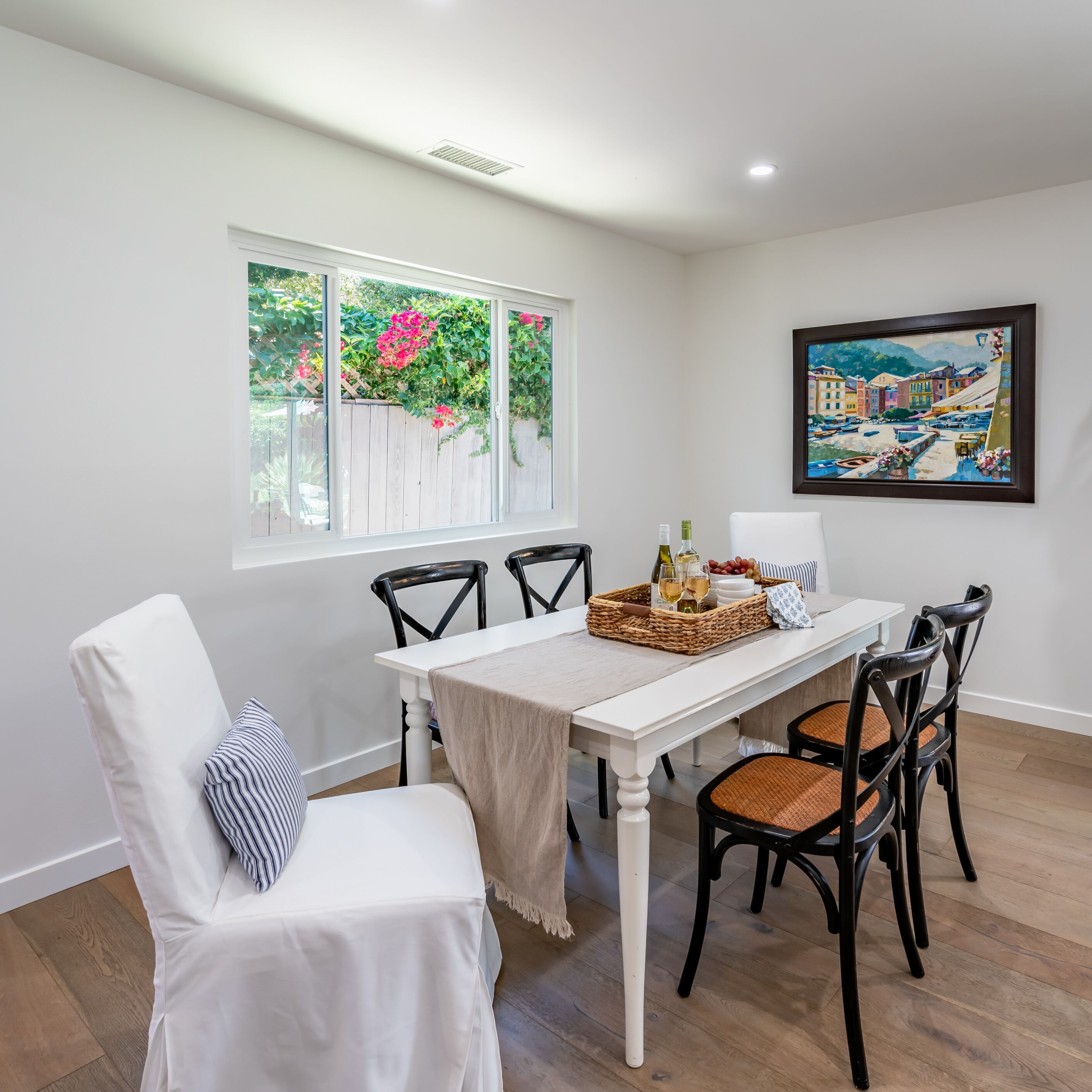A dining area with a white table, black chairs, and a painting on the wall.