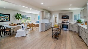 A spacious kitchen with modern appliances, a dining area with a large table and chairs, and a view of the outdoors. - Barefoot Retreat - Upscale Living on the Mesa (Santa Barbara)