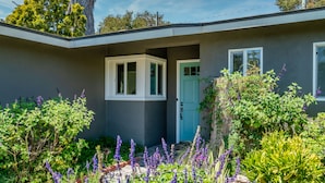 A modern house with a grey exterior, a blue door, and a small garden with purple flowers. - Barefoot Retreat - Upscale Living on the Mesa (Santa Barbara)