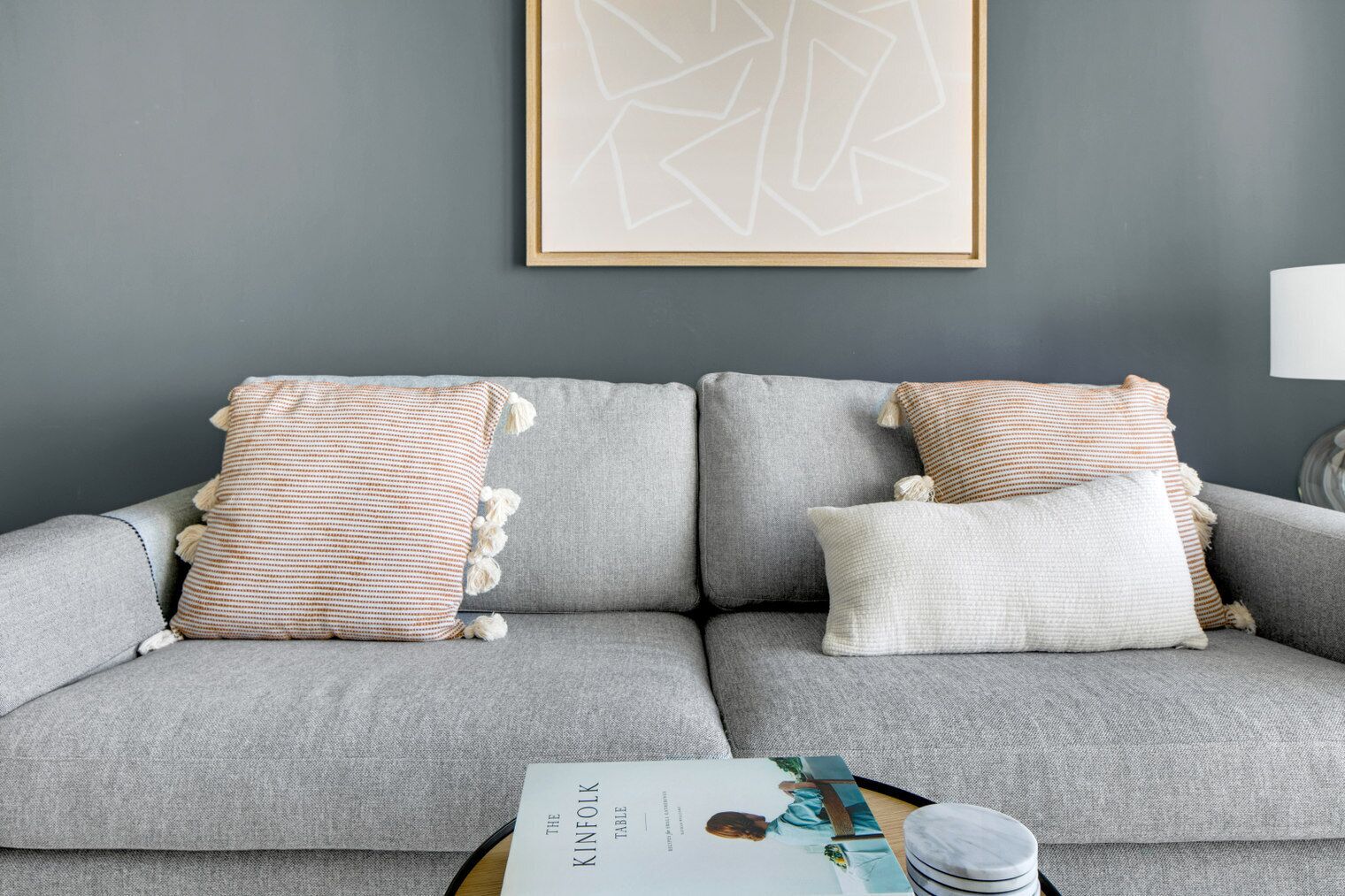 Ein graues Sofa mit gestreiften und einfarbigen Kissen, ein gerahmtes abstraktes Kunstwerk darüber und eine Zeitschrift auf einem Beistelltisch.