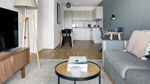 A modern living room with a flat-screen TV, a lamp, a sofa, and a coffee table with books and a stack of plates. - Elegant Landstraße 1BR w/ Elevator & Playglound, Calm Area, by Blueground (Vienna)