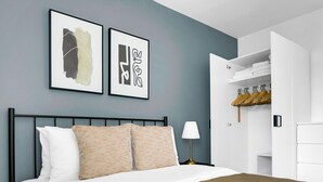 A modern bedroom with a bed, two framed artworks, a bedside lamp, and a wardrobe with hanging clothes. - Elegant Landstraße 1BR w/ Elevator & Playglound, Calm Area, by Blueground (Vienna)
